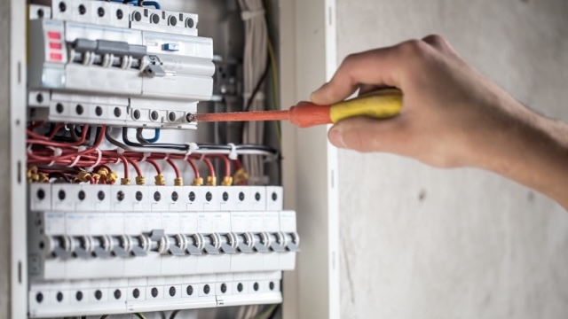 Man, an electrical technician working in a switchboard with fuses. Installation and connection of electrical equipment. Professional with tools in hand. concept of complex work, space for text.